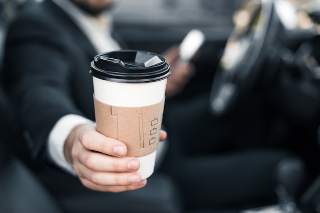 Hübscher kaukasischer Geschäftsmannfahrer innen im Fahrzeug mit Kaffee und Gadget und Scheckpost und im Gespräch mit Partnern