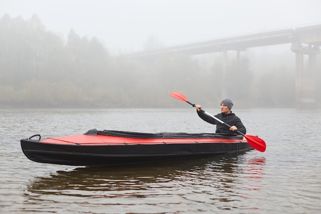 Hübscher Kerl mit Ruder in Händen rudert sein Boot und schaut in die Ferne