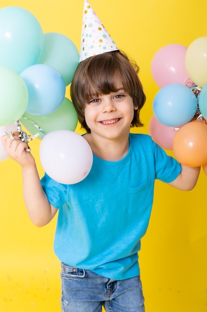 Hübscher kleiner Geburtstagskind in blauem Hemd und Hut mit Luftballons auf gelbem Hintergrund alles Gute zum Geburtstag