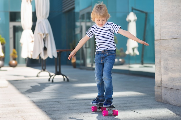 Hübscher kleiner Junge auf einem Skateboard. Emotionales Kind im Freien. Nettes Kind, das Sonnenbrille trägt.