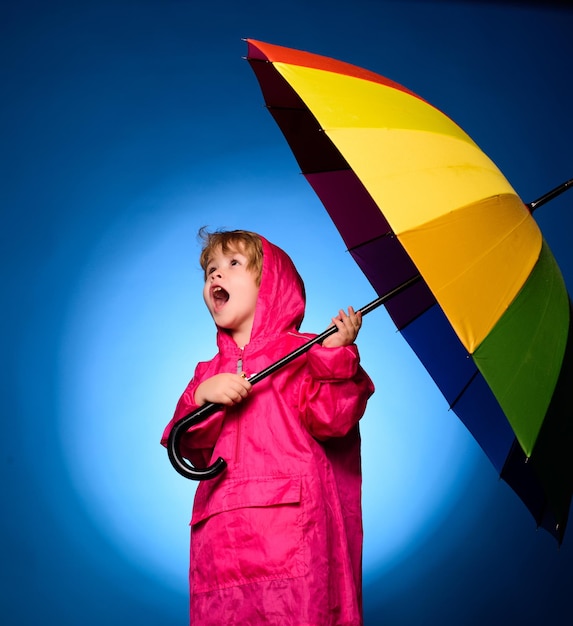 Hübscher kleiner Kerl bei der Vorbereitung auf den Herbst Fröhlicher Junge im Regenmantel mit buntem Regenschirm Kind im Regen Wolke Regenschirm Regenkonzept Kind werben für Ihr Produkt und Ihre Dienstleistungen Lustiges Gesicht