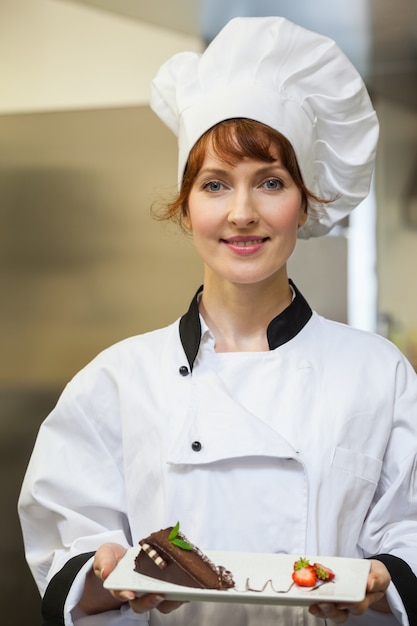 Hübscher lächelnder Chef, der Schokoladenkuchen mit Erdbeeren darstellt