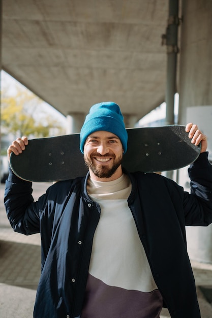 Hübscher lächelnder europäischer Skater, der mit einem Skateboard in den Händen posiert Vertikales Foto Hochwertiges Foto