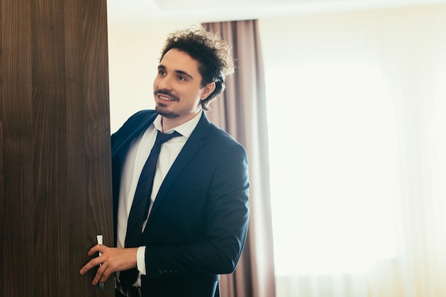 Hübscher lächelnder Geschäftsmann, der Kleiderschrank im Hotelzimmer öffnet