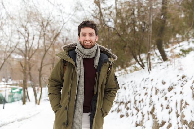 Hübscher lächelnder junger Mann, der Winterjacke trägt, die draußen geht