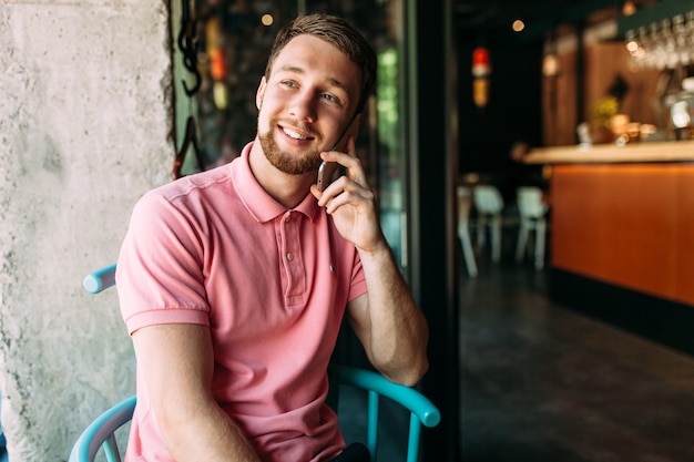 Hübscher lächelnder Mann, der in einem Café sitzt und am Telefon spricht, Hipster