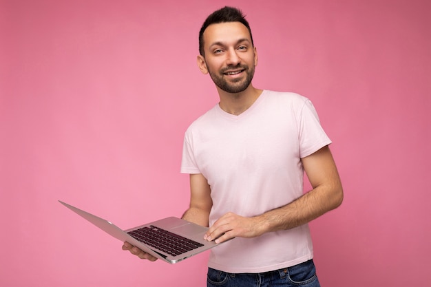 Hübscher lächelnder Mann, der Laptop-Computer hält und Kamera im T-Shirt betrachtet