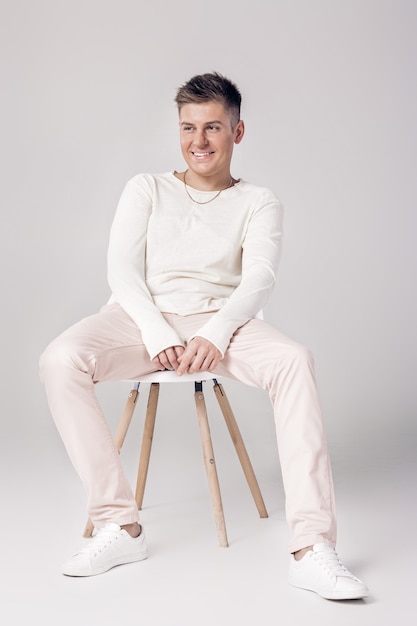 Hübscher lächelnder Mann im weißen Pullover und in der Hose sitzt auf einem Stuhl