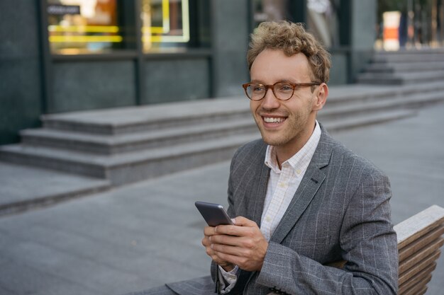 Hübscher lächelnder Mann mit Brille mit Handy-Shopping online mit Blick auf den Kopierraum