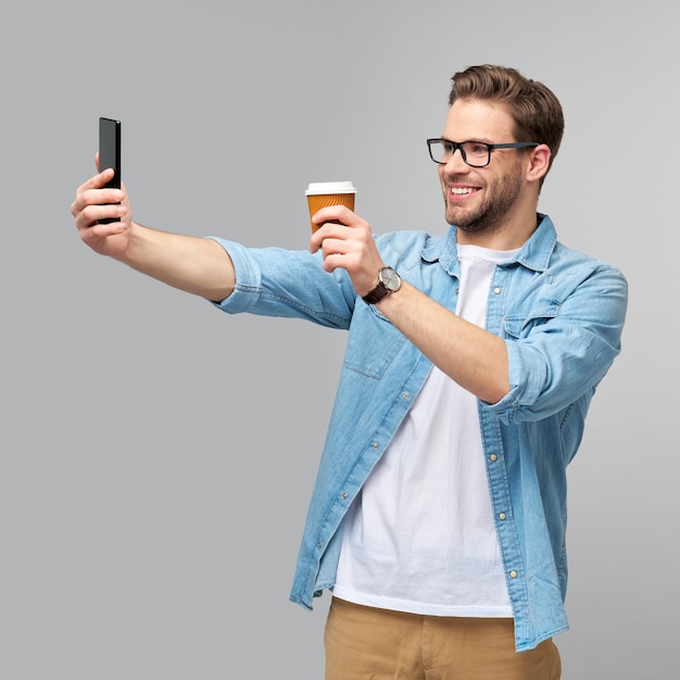 hübscher lässiger Mann im blauen Jeanshemd, der sein Telefon und eine Tasse Kaffee hält, um zu gehen