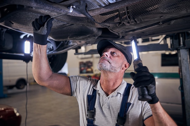 Hübscher männlicher Arbeiter, der Auto in der Autowerkstatt repariert