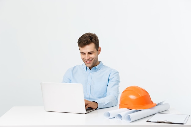 Hübscher männlicher Bauingenieur, der im Büro mit Laptop arbeitet