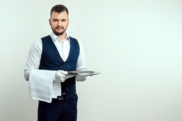 Hübscher männlicher Kellner im weißen Hemd, der ein silbernes Tablett hält. Das Konzept des Servicepersonals, das Kunden in einem Restaurant bedient.