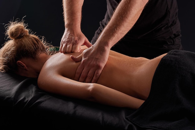 Foto hübscher männlicher masseur, der ein mädchen auf schwarzem hintergrund massiert. konzept der therapeutischen entspannenden massage