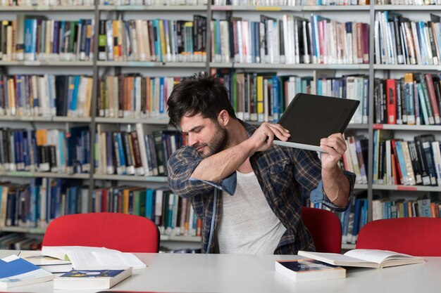 Hübscher männlicher Student, der Laptop wirft und ihn zerstören will