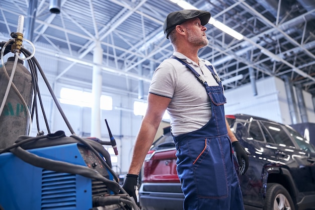 Hübscher männlicher Techniker in Arbeitsoveralls mit professioneller Automobilausrüstung an der Autoreparatur-Servicestation