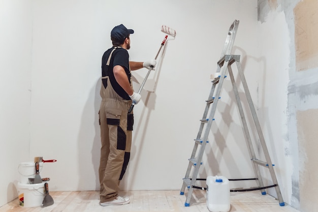 Hübscher Maler mit Farbroller im leeren Raum malt die Wand