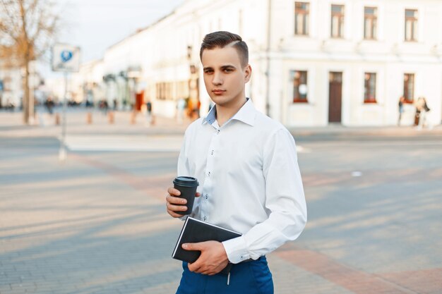 Hübscher Manager Mann mit Kaffee und Notizblock, der in der Stadt geht