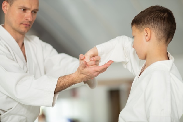 Hübscher Mann, der kleine Jungen Aikido-Bewegungen lehrt