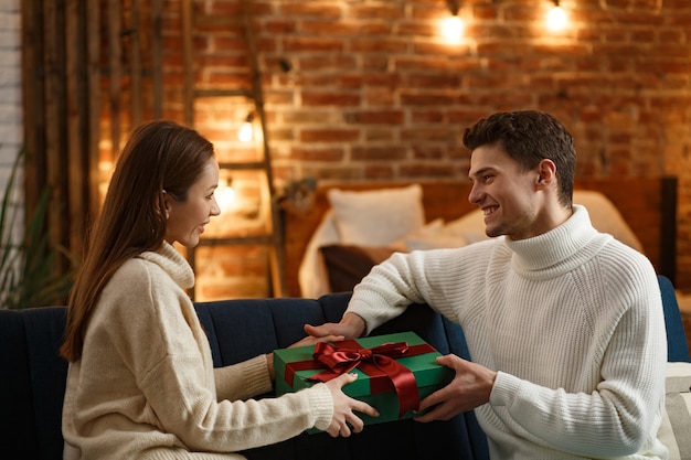 Hübscher Mann, der seinem schönen Mädchen ein Geschenk präsentiert und lächelt