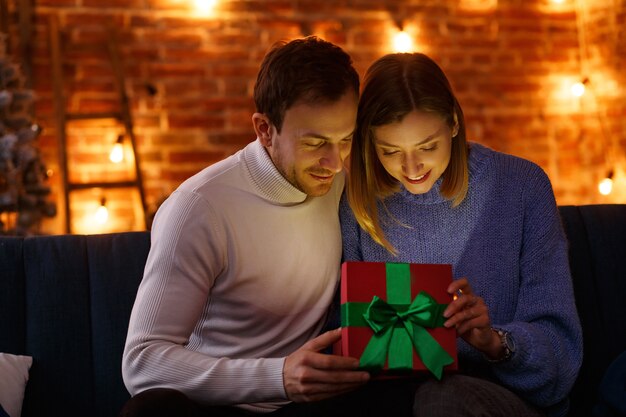 Hübscher Mann, der seiner schönen Frau ein Geschenk präsentiert und lächelt