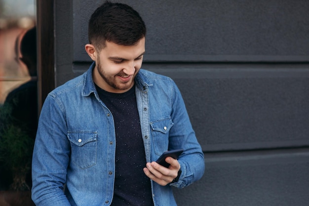 Hübscher Mann in einem Jeanshemd benutzt ein Telefon, das auf der Straße steht