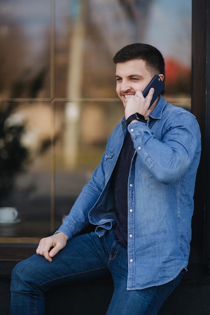 Hübscher Mann in einem Jeanshemd benutzt ein Telefon, das auf der Straße steht