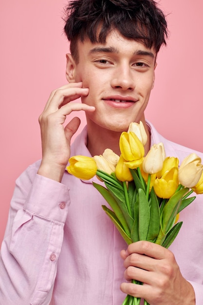 Hübscher Mann in einem rosa Hemd mit einem Blumenstrauß, der mit seinen Händen gestikuliert rosa Hintergrund unverändert