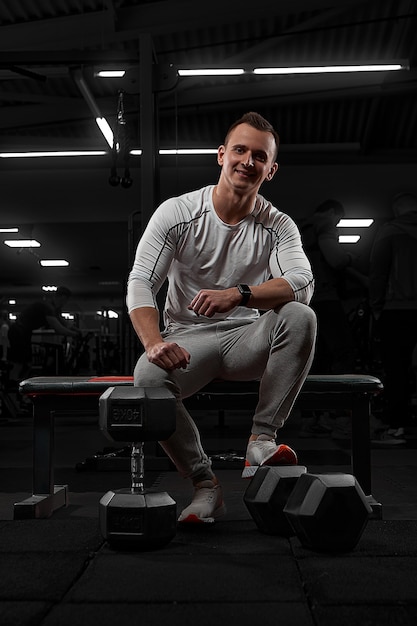 Hübscher Mann mit großen Muskeln, der an der Kamera im Fitnessstudio aufwirft. Modell in weißer Sportbekleidung