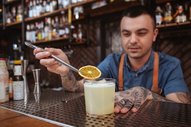 Hübscher Mann tätowierte den Barmixer, der ein Getränk vorbereitet