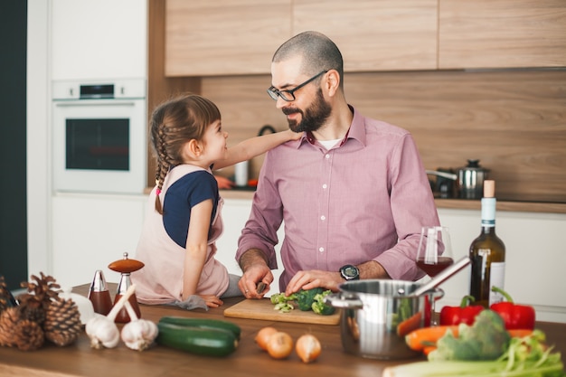 Hübscher Mann und seine süße kleine Tochter kochen zusammen Gemüseeintopf in der Küche. Gesundes und vegetarisches Lebensmittelkonzept.