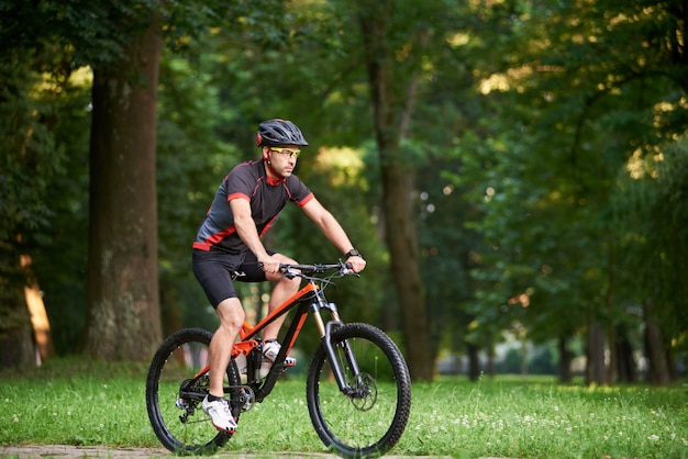 Hübscher Mannbiker, der auf dem Fahrrad trainiert und sich auf das Rennen im Park an der frischen Luft vorbereitet. Mann, der Morgenradtour genießt. Motivationskonzept, gesunder Lebensstil