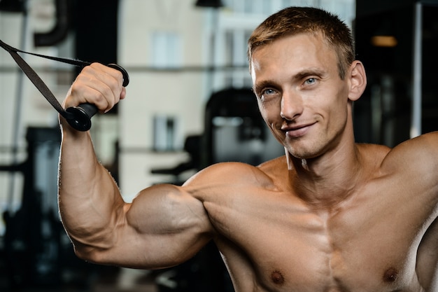 Hübscher Modell junger Mann, der Arme im Fitnessstudio trainiert