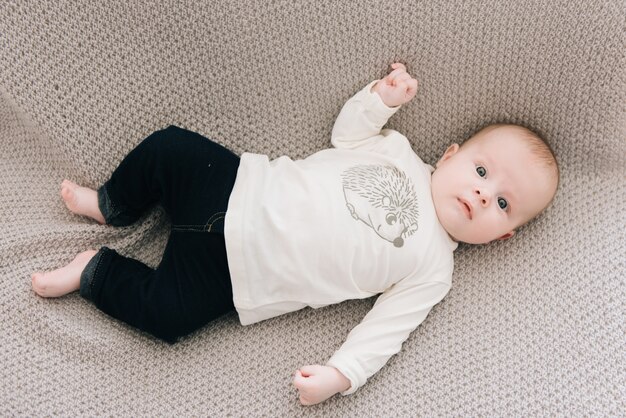 Hübscher modischer kleiner Junge, der auf einer Decke liegt, mit einem süßen Ausdruck