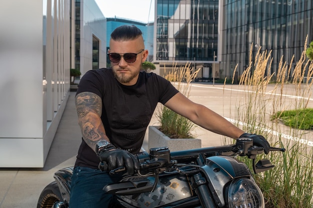 Foto hübscher motorradfahrer mit sonnenbrille auf seinem motorrad vor urbaner kulisse, während er durch die stadt fährt