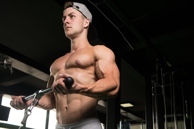 Hübscher muskulöser Fitness-Bodybuilder, der schwere Übungen für Bizeps an der Maschine mit Kabel im Fitnessstudio macht