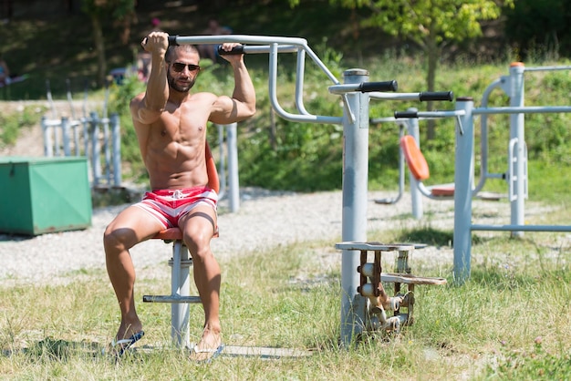 Hübscher muskulöser junger Mann beim Training auf dem Spielplatz im Park