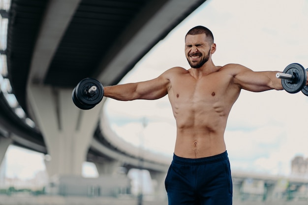 Hübscher muskulöser Mann mit nacktem Oberkörper im Freien, der Fitness-Training tut