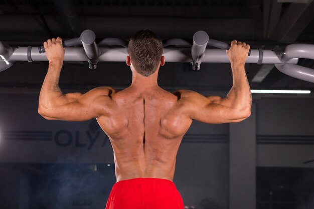 Hübscher muskulöser Mann mit perfektem Körper, der Klimmzüge im Fitnessstudio tut