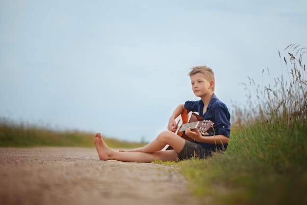 Hübscher netter Junge spielt auf Akustikgitarre sittingon Straße am Sommertag.