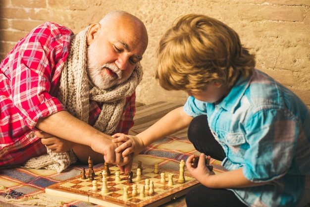 Hübscher Opa und Enkel spielen Schach, während sie zu Hause Zeit miteinander verbringen. Schachhobby-Opa mit Enkel beim Schachspielen