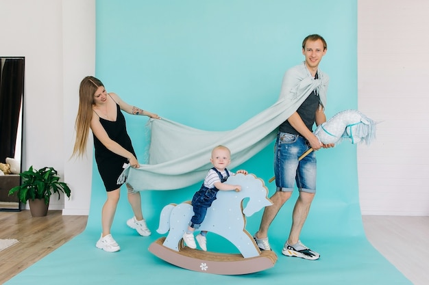 Foto hübscher prinz und schicke prinzessin mit kleinem sohn, prinz auf spielzeugpferd und kariertem regenmantel