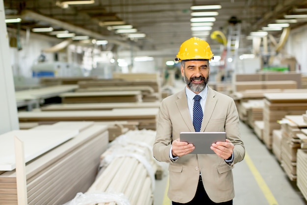 Hübscher reifer Ingenieur in der Fabrik mit digitaler Tablette