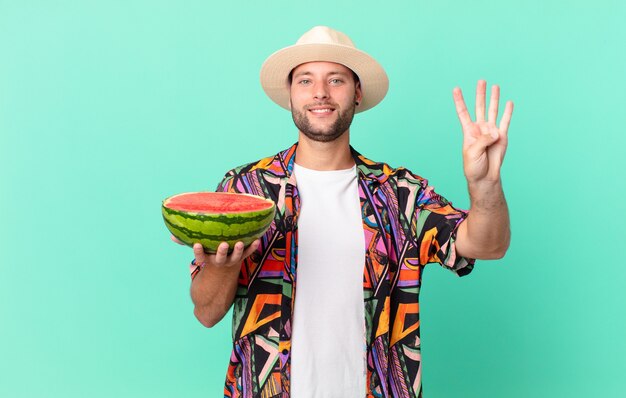 Hübscher reisender Mann, der freundlich lächelt und aussieht, Nummer vier zeigt und eine Wassermelone hält. Urlaubskonzept