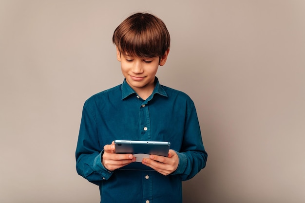 Hübscher, ruhiger Teenager im blauen Hemd hält ein Tablet in der Hand und spielt damit