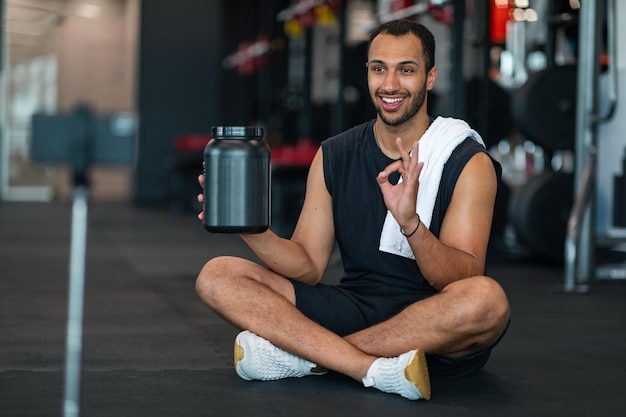 Hübscher schwarzer männlicher Athlet, der im Fitnessstudio eine Videobewertung für Molkepulver erstellt