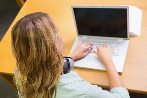 Hübscher Student, der in der Bibliothek mit Laptop studiert