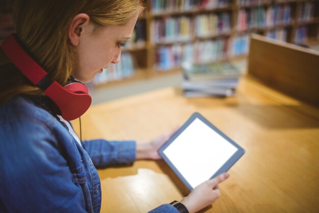 Hübscher Student mit den Kopfhörern, die Tablette in der Bibliothek verwenden