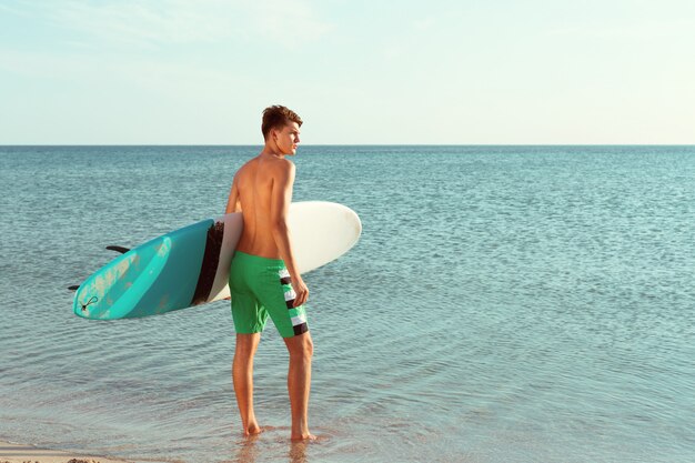 Hübscher Surfer, der sein Surfbrett hält