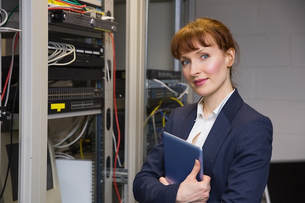 Hübscher Techniker, der an der Kamera neben dem offenen Server hält Tabletten-PC lächelt